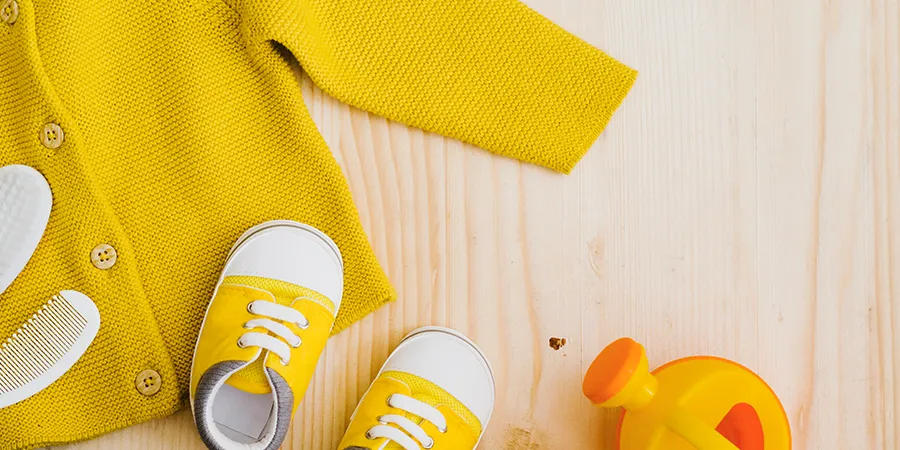 Slika odozgo bebi obuce i dzempera, jaorko zute boje, na drvenom podu.
