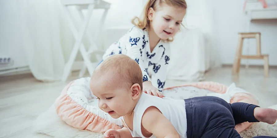 Mala devojčica se igra sa svojom mlađom (bebom) sestrom na podu.