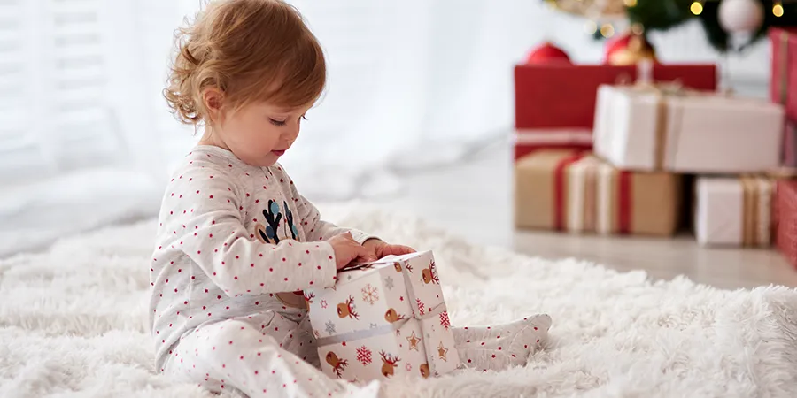 Mala devojčica u pidžami, otvara svoj poklon na belom tepihu.