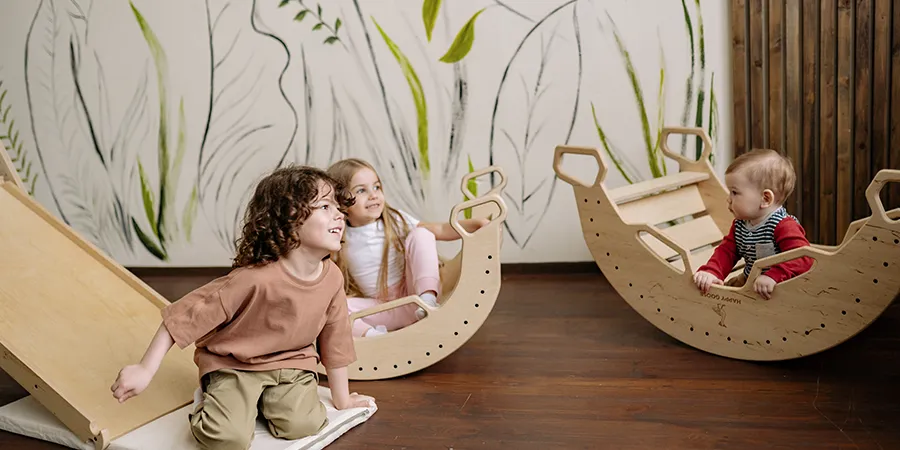 Troje male dece se igraju u lepo dekorisanoj sobi sa drvenim toboganom i klackalicama.