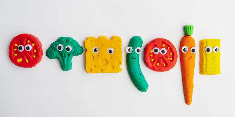 Raznobojne igračke za žvakanje u obliku povrća, na beloj pozadini.