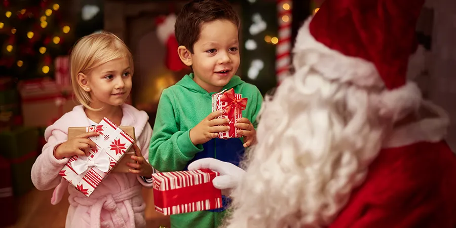 Dečak i devojčica oduševljeno primaju poklone od Deda Mraza.