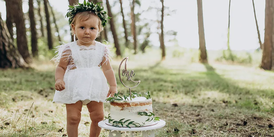 Preslatka devojčica u beloj haljini sa svojom prvom rođendanskom tortom u prirodi.