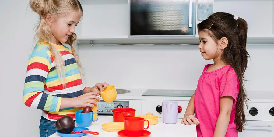 Dve devojčice se igraju sa kuhinjom za decu.