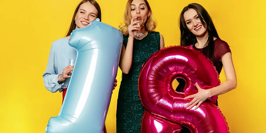 Tri mlade devojke sa pičem u rukama na žutoj pozadini. Dve devojke drže balone u obliku brojeva 1 i 8.