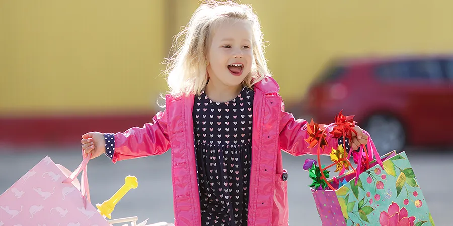 Slatka, nasmejana devojčica plave kose, veselo šeta sa ukransim kesama punim poklonima.