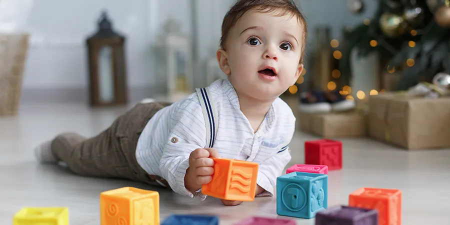 Slatki dečak od par meseci se igra kockicama na podu u svom stanu.