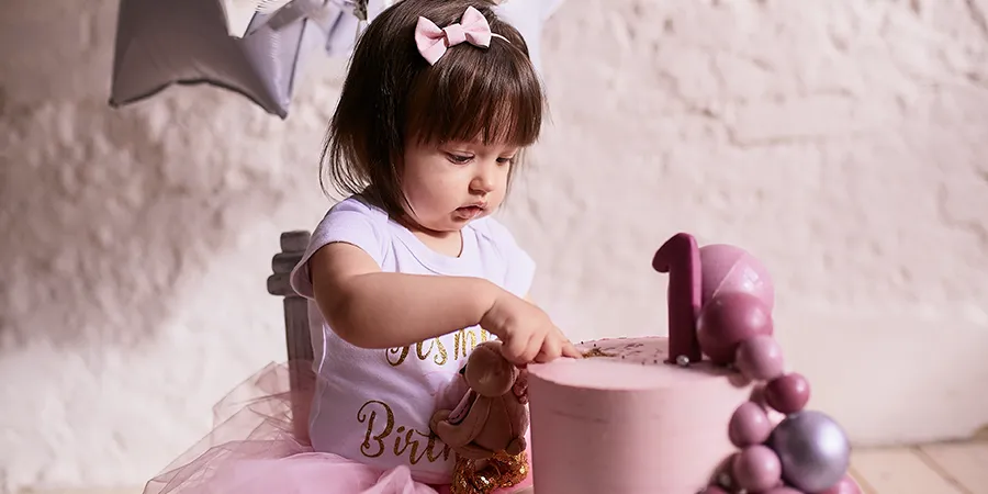 Preslatka devojčica sedi u maloj, dečijoj stolici i prstićem načinje slavljeničku tortu.