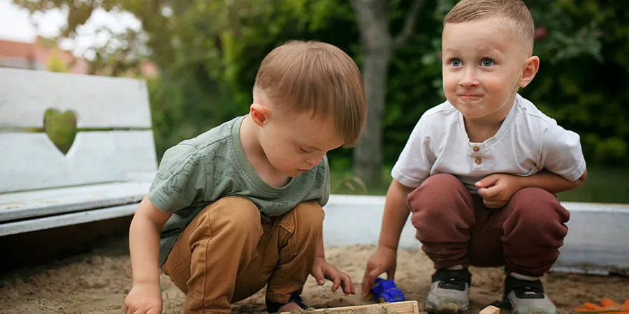 Dva mala dečaka smeđe kose, igraju se u pesku.