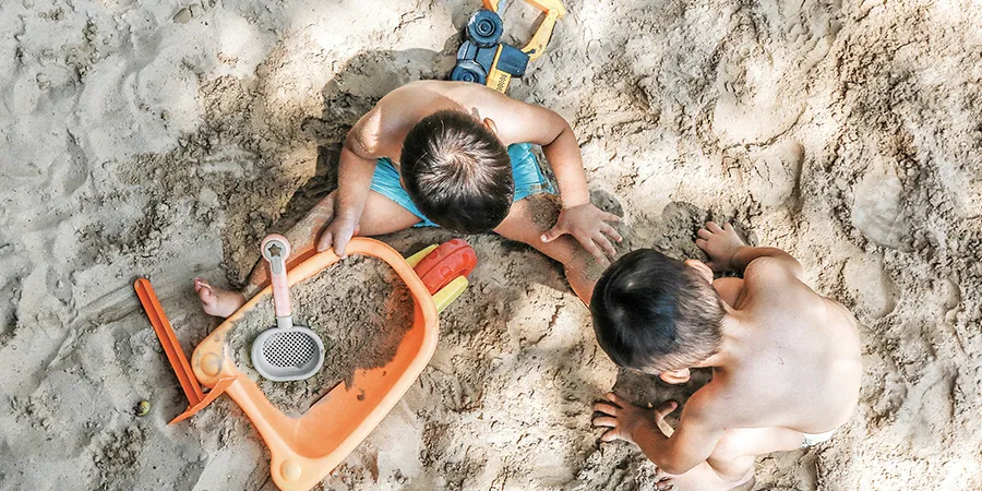 Kadar odozgo - dva dečaka se igraju u pesku plastičnim igračkama.