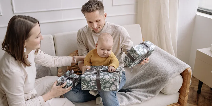 Kadar srećne porodice. Mama, tata i beba sede na sofi sa poklonima u rukama.