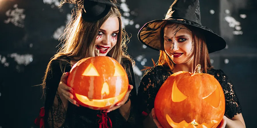 Dve devojčice, maskirane u veštice, sa rezbarenim bundevama u rukama, poziraju za Noć veštica.