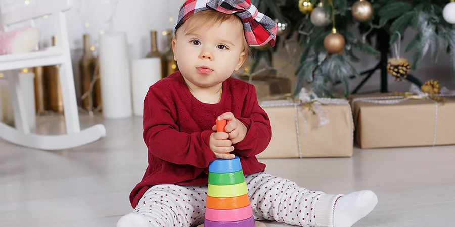 Mala devojčica sedi na podu, ispred novogodišnje jelke i igra se svojom igračkom.