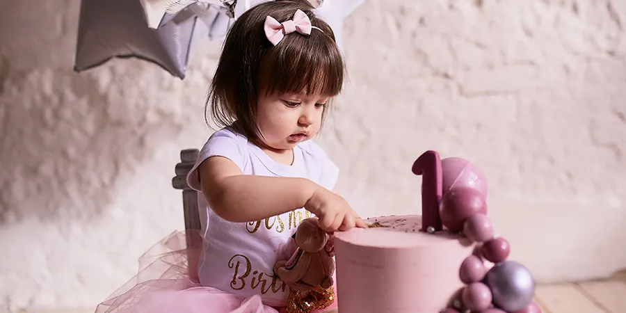 Slatka devojčica, u roze haljini sedi na maloj, dečijoj stolici i otvara poklone.