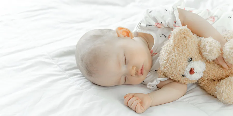 Beba spava ne beloj posteljini sa plišanim medom u zagrljaju.