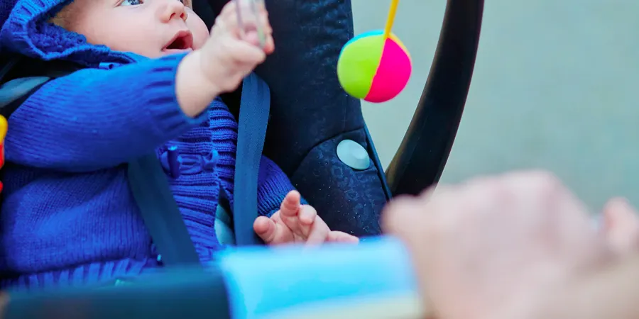 Beba u kolicima poseže za igračkom koja visi ispred nje.
