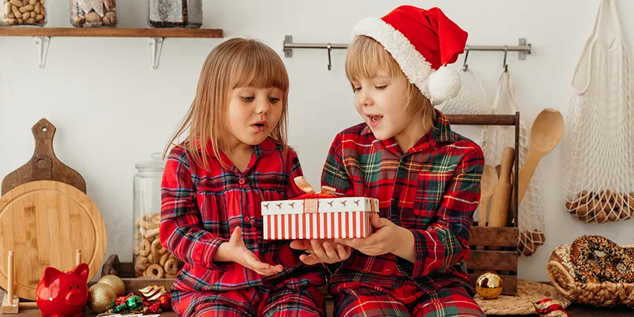 Dve male devojčice, sede na radnom delu kuhinje i zajedno drže novogodišnji poklon.