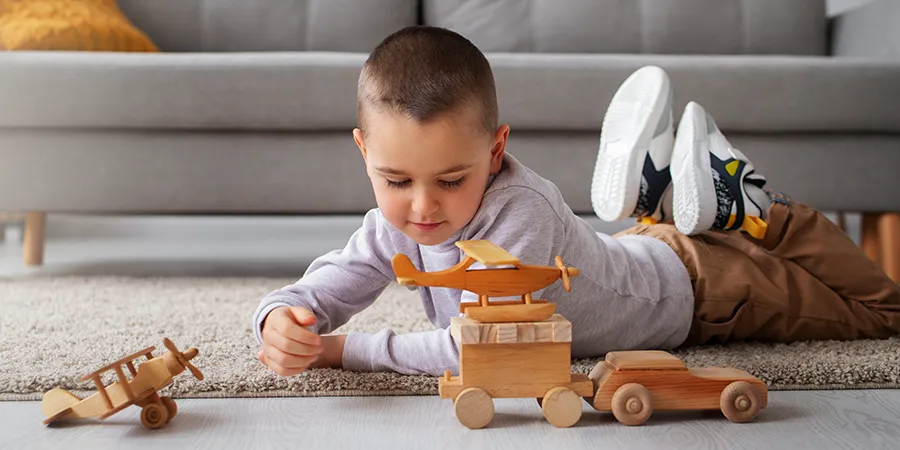 Dečak se na podu igra drvenim automobilom i avionima.