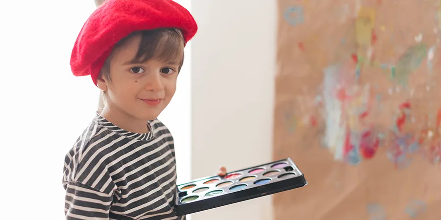 Dečak sa slikarskom kapicom drži boje za slikanje u ruci.