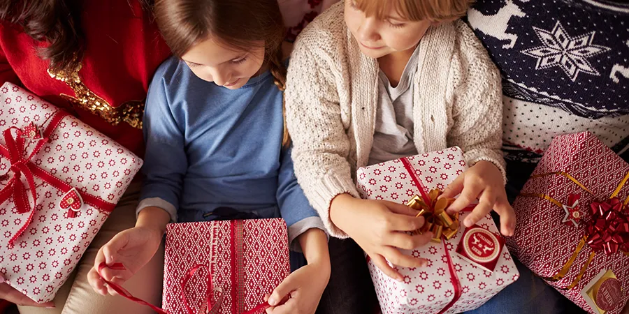Dečak i devojčica otvaraju svoje poklone doke sede između roditelja. Kadar odozgo.