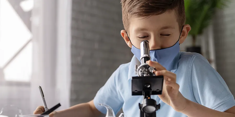 Krupni kadar dečaka koji gleda kroz svoj mikroskop.