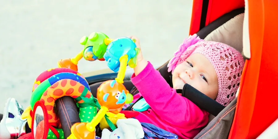 Devojčica, obučena u roze, gleda u kameru dok sedi u kolicima punim igračkama.