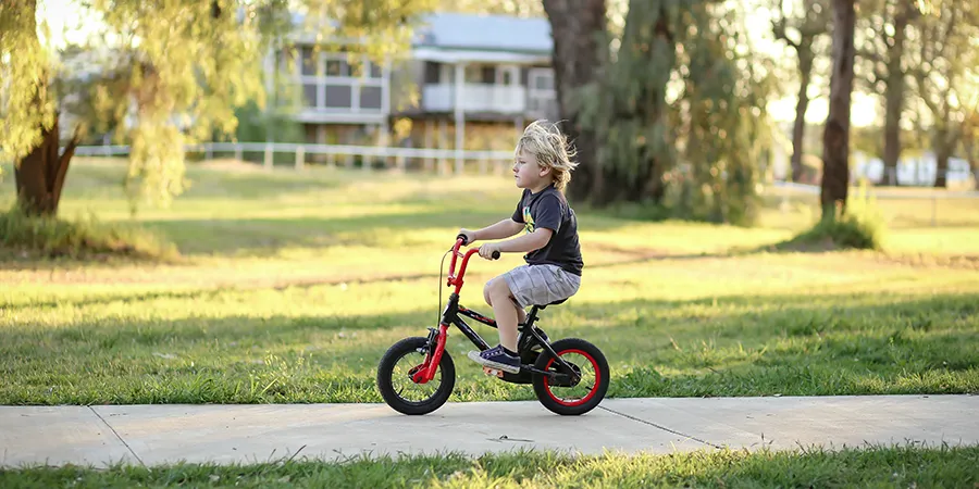 Plavokosi dečak vozi biciklo po lepom letnjem danu.