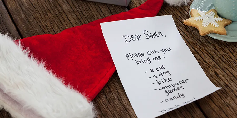 Pismo Deda Mrazu na drvenom stolu. U kadru je i novogodišnja kapa.