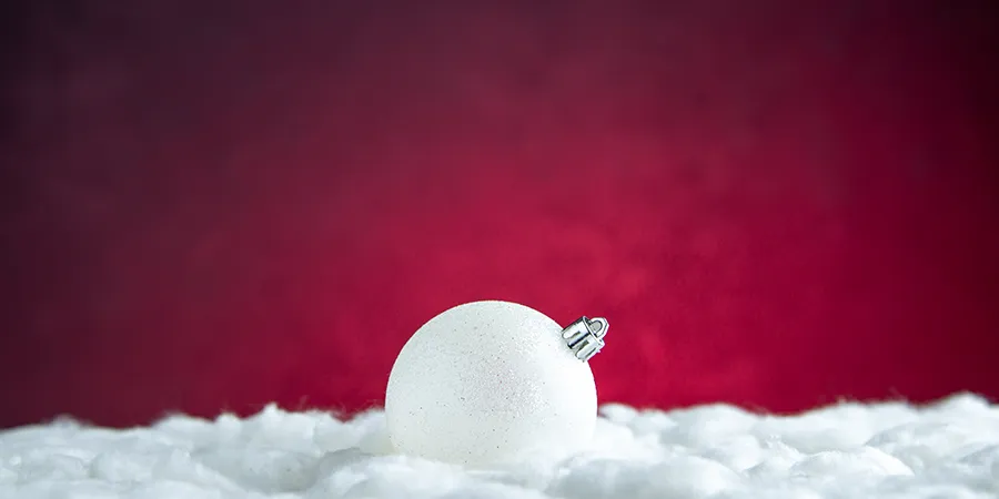 Beli ukras za jelku na veštačkom snegu, sa crvenom pozadinom.
