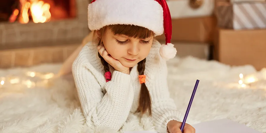 Krupni kadar devojčice sa novogodišnjom kapicom koja pise na podu.