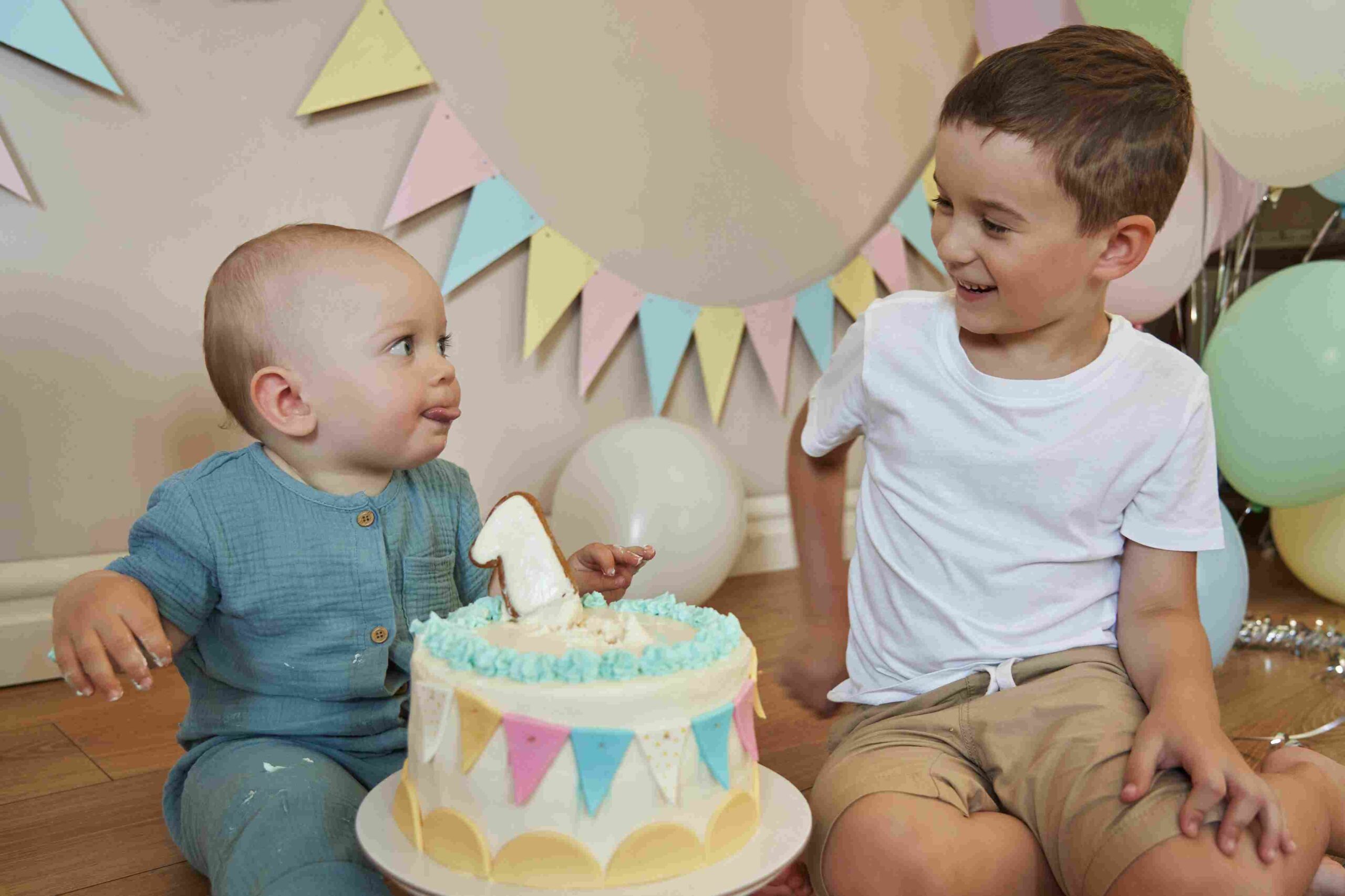 Dvoje male dece sede pored rođendanske torte i smeju se tokom proslave